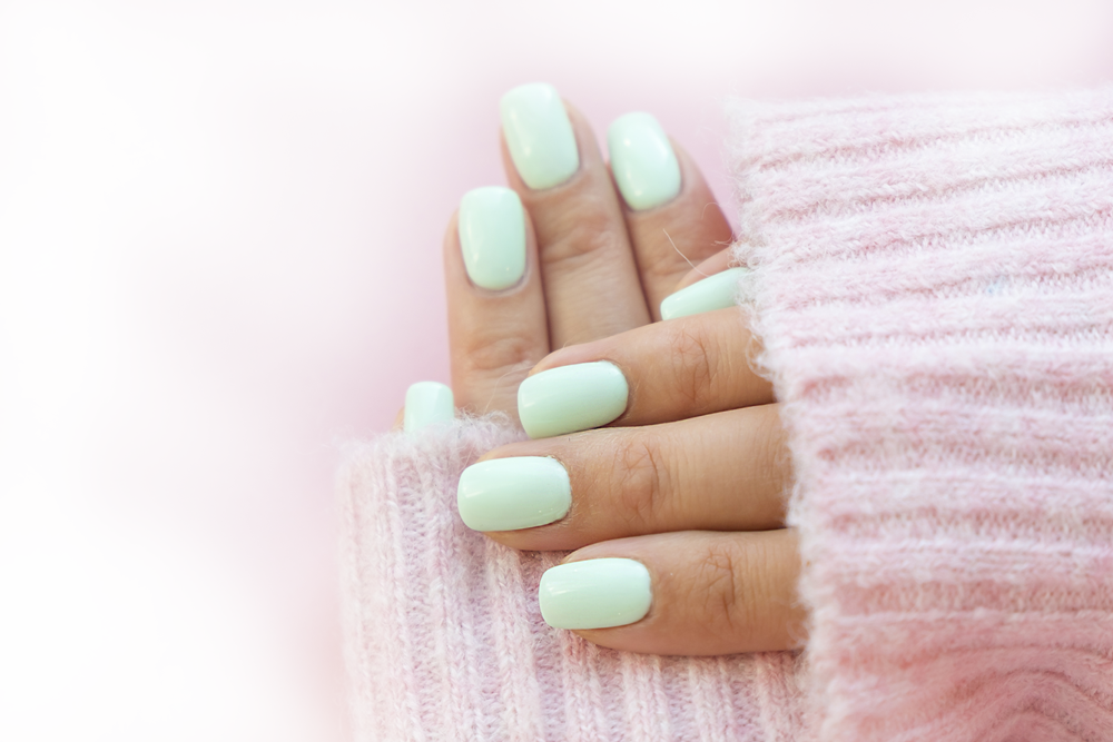 mains de femme manucurées avec unvernis vert léger pull rose 